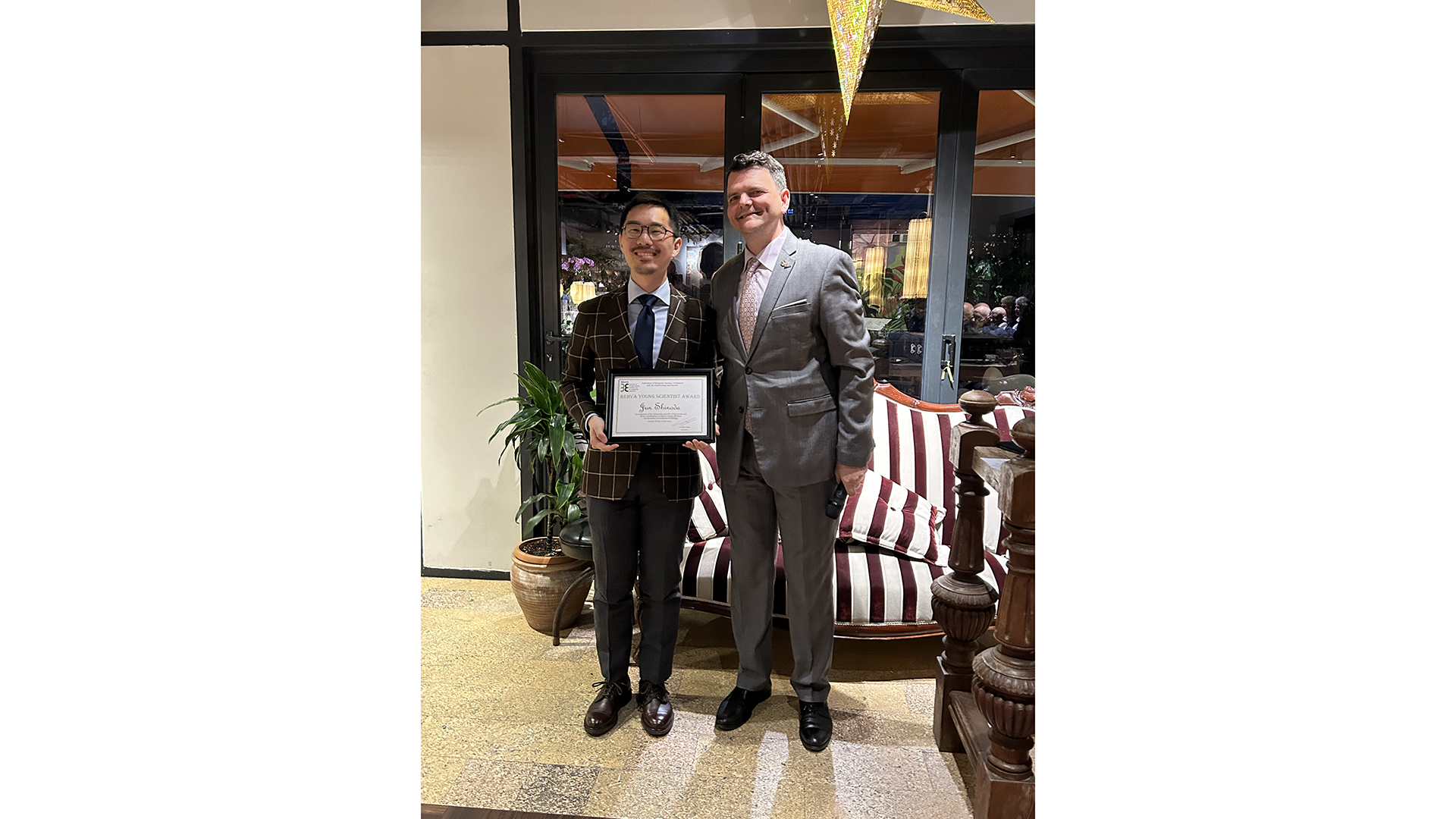 Two gentleman posing for a photo where the one on the left is holding a diploma